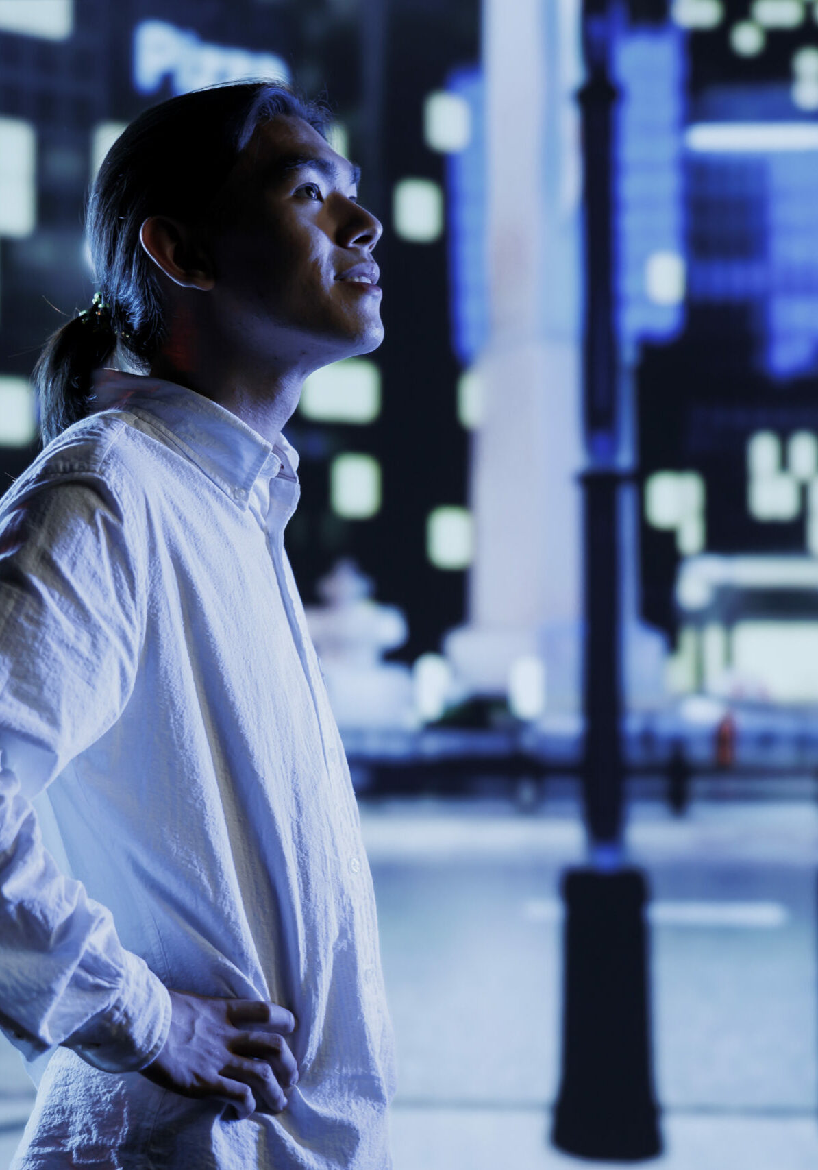 Asian man wandering around city boulevards during nighttime, being amazed by urban landscape buildings. Citizen strolling around empty avenues at night, enjoying street lamps illuminated surroundings